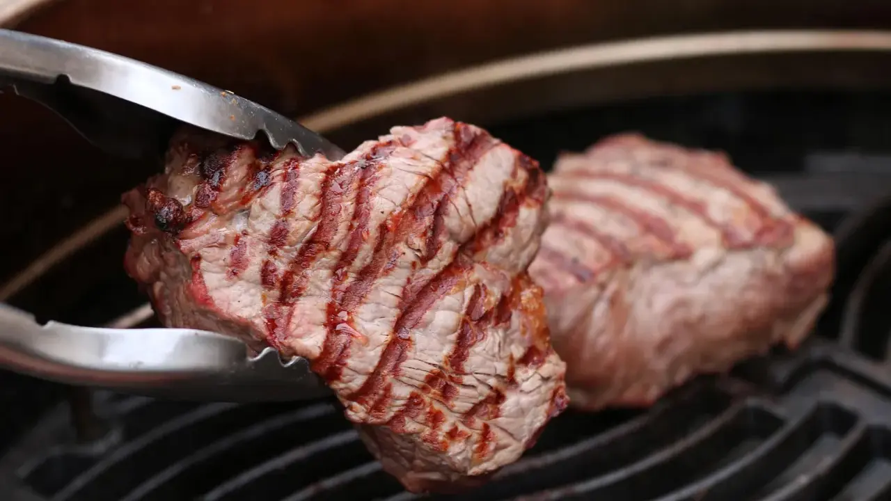 Zangen halten ein saftiges Stück Roastbeef, das auf einem Grill zubereitet wird.