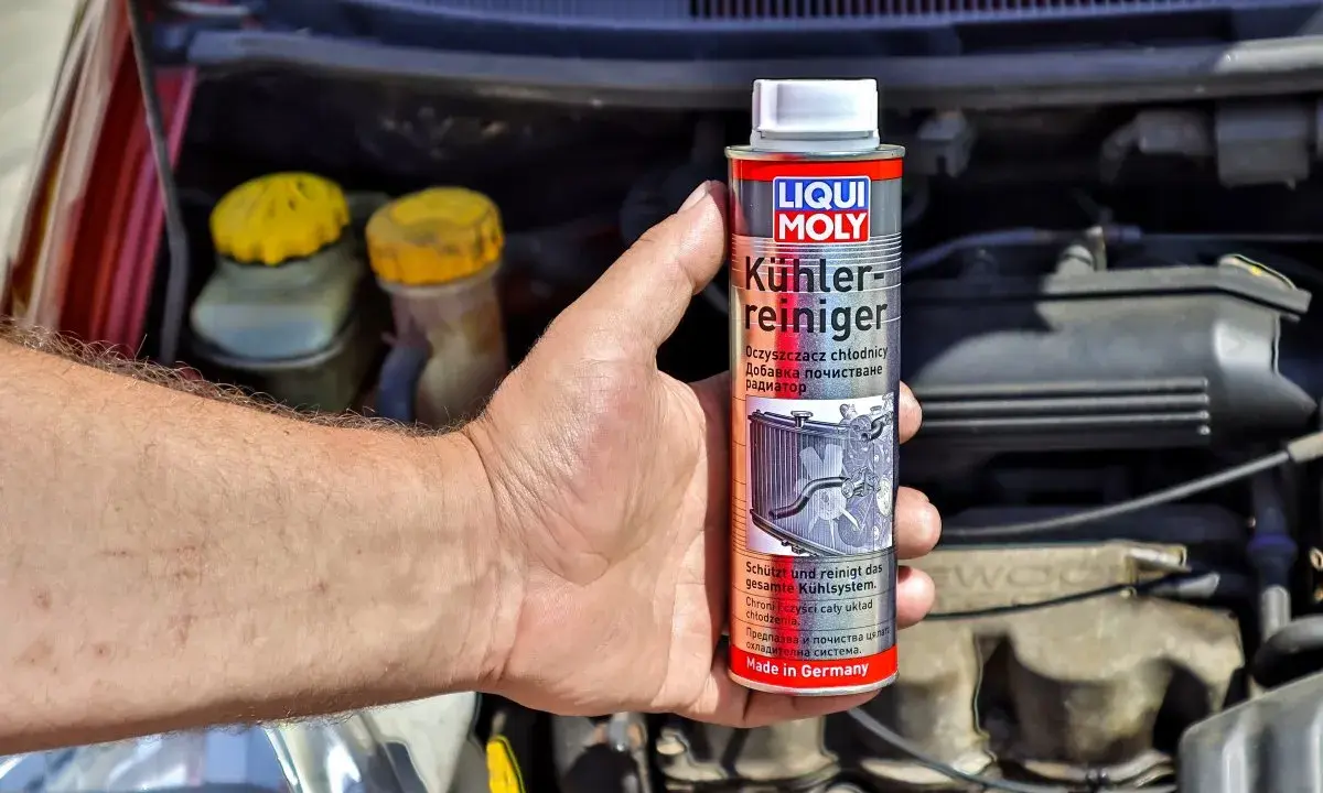 Dłoń trzyma puszkę preparatu Liqui Moly do płukania układu chłodzenia. W tle widać silnik samochodu.