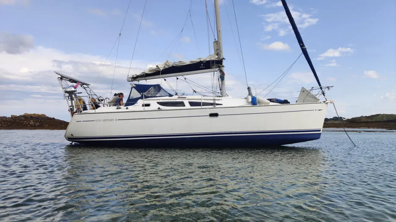 Un voilier Sun Odyssey 35, blanc avec une bande bleue, navigue paisiblement sur une mer calme. Les avis sur ce bateau sont positifs.