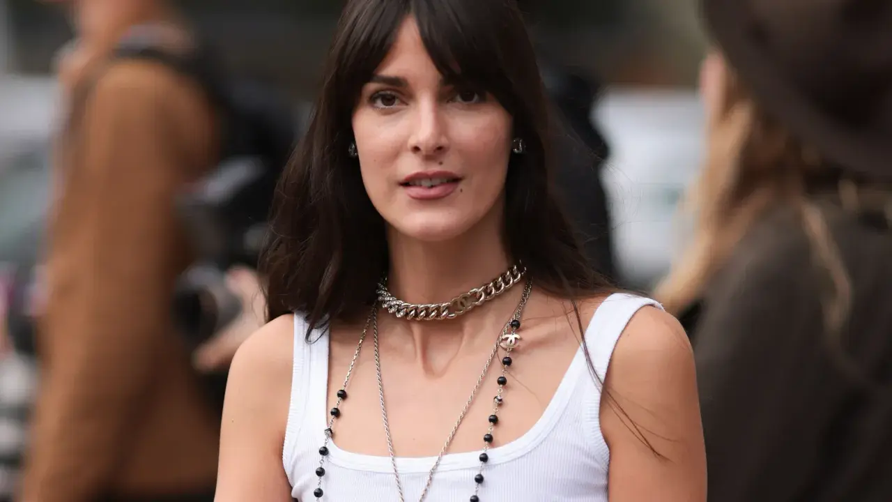 Frau mit langen Haaren und Curtain Bangs, trägt weiße Tanktop und Chanel-Schmuck.