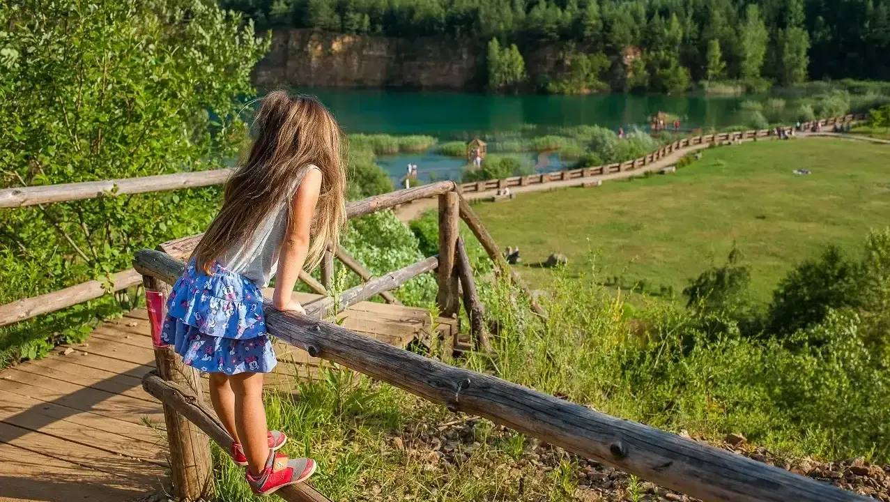 Dziewczynka na drewnianej kładce podziwia Park Gródek Jaworzno. Warto sprawdzić cenę wstępu, by cieszyć się tym widokiem!