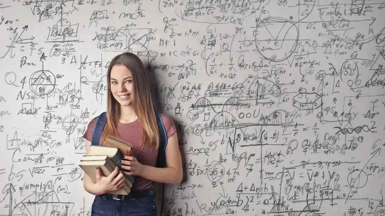 Uśmiechnięta studentka z książkami przed ścianą pełną równań matematycznych. Zastanawia się, co po studiach matematycznych.
