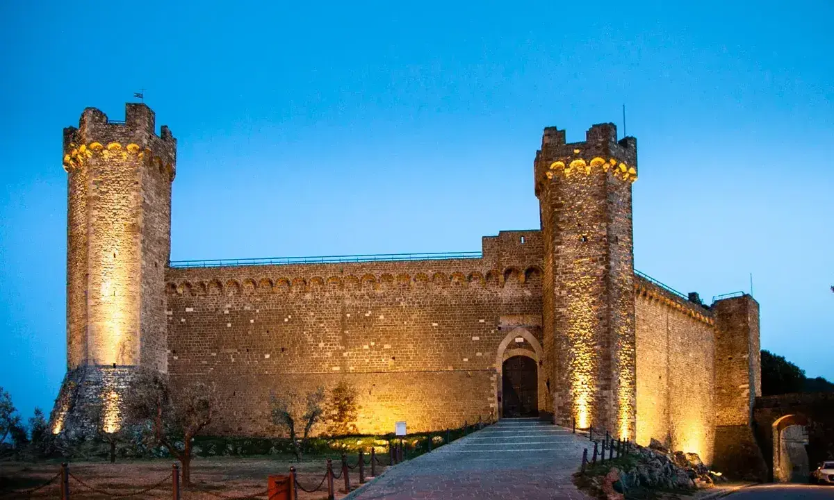 Fortezza illuminata al crepuscolo, simbolo del centro storico di Montalcino. Un'antica roccaforte che domina il paesaggio toscano.
