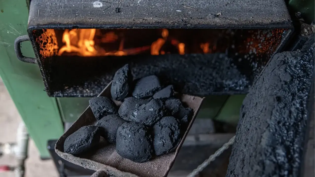Łopata z węglem brunatnym czeka na załadunek do pieca węglowego. W palenisku żarzą się płomienie, gotowe do ogrzania domu.