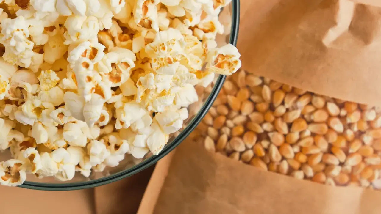 Miseczka pełna puszystego popcornu obok woreczka z ziarnami kukurydzy. Czy popcorn jest lekkostrawny? Zależy od dodatków!