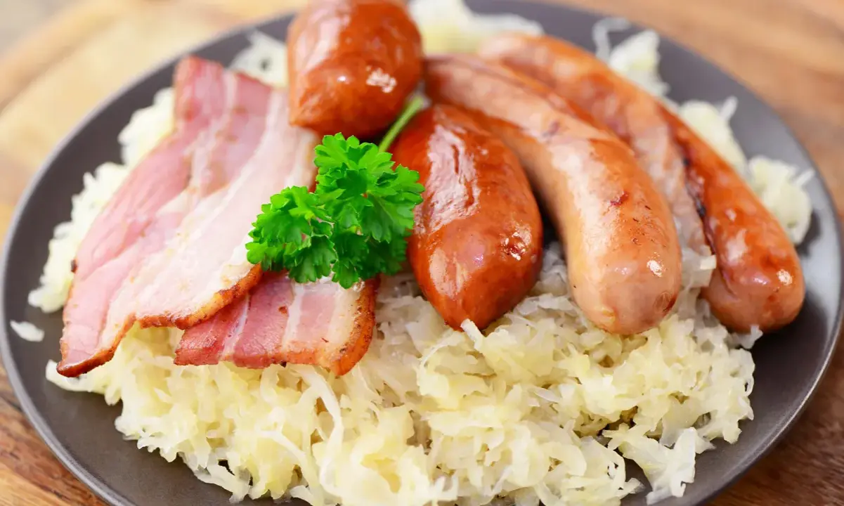 Assiette de choucroute allemande ou alsacienne garnie de saucisses et de lardons, décorée d'une touche de persil frais.