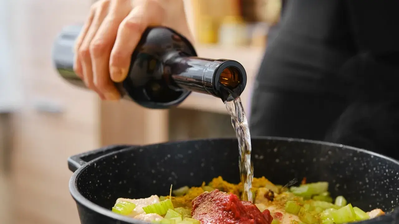 Una mano vierte vino en una sartén con ingredientes. El vino en moderación realza el sabor de la comida.