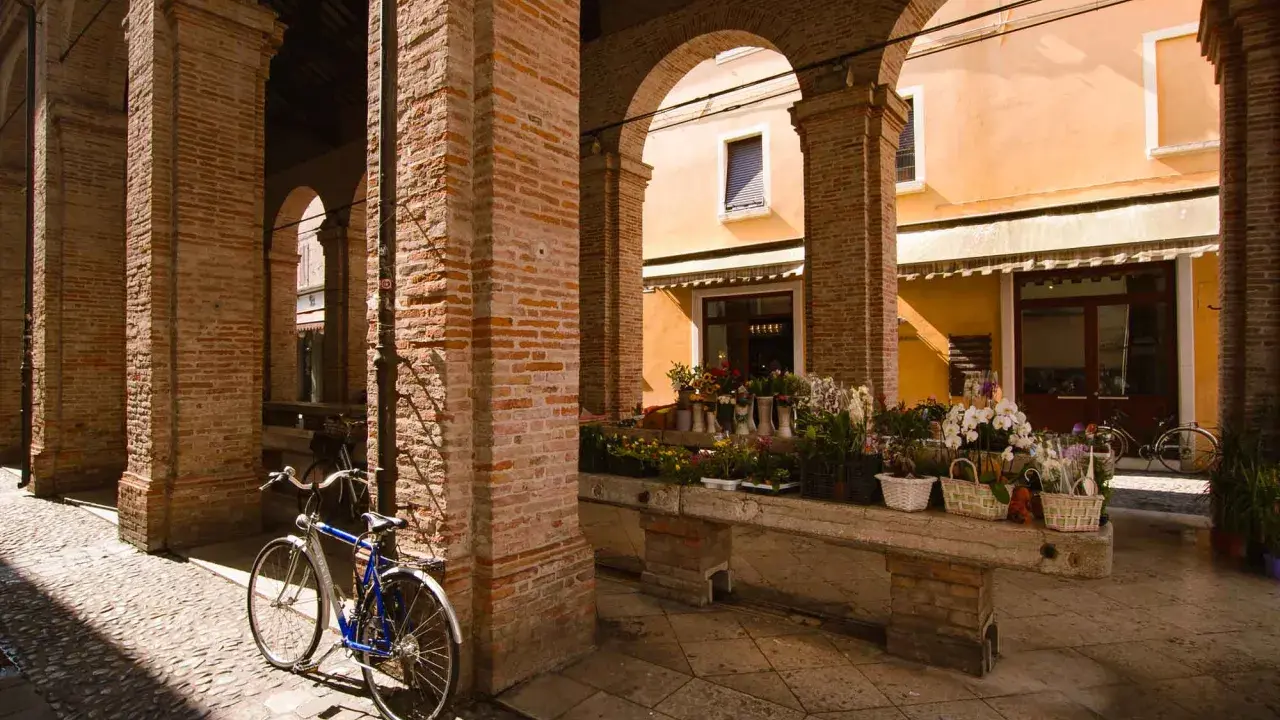 Sotto gli archi di mattoni rossi, un tempo la vecchia pescheria, ora un fiorista espone i suoi colori. Una bicicletta blu riposa sul selciato.