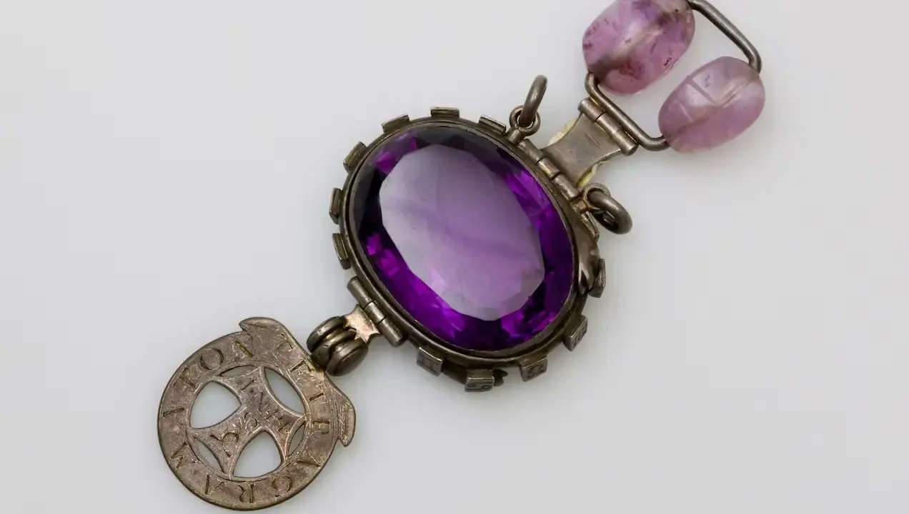 Un ciondolo con grande ametista centrale, due perle rosa e un simbolo inciso. Si dice che l'ametista porti sfortuna.
