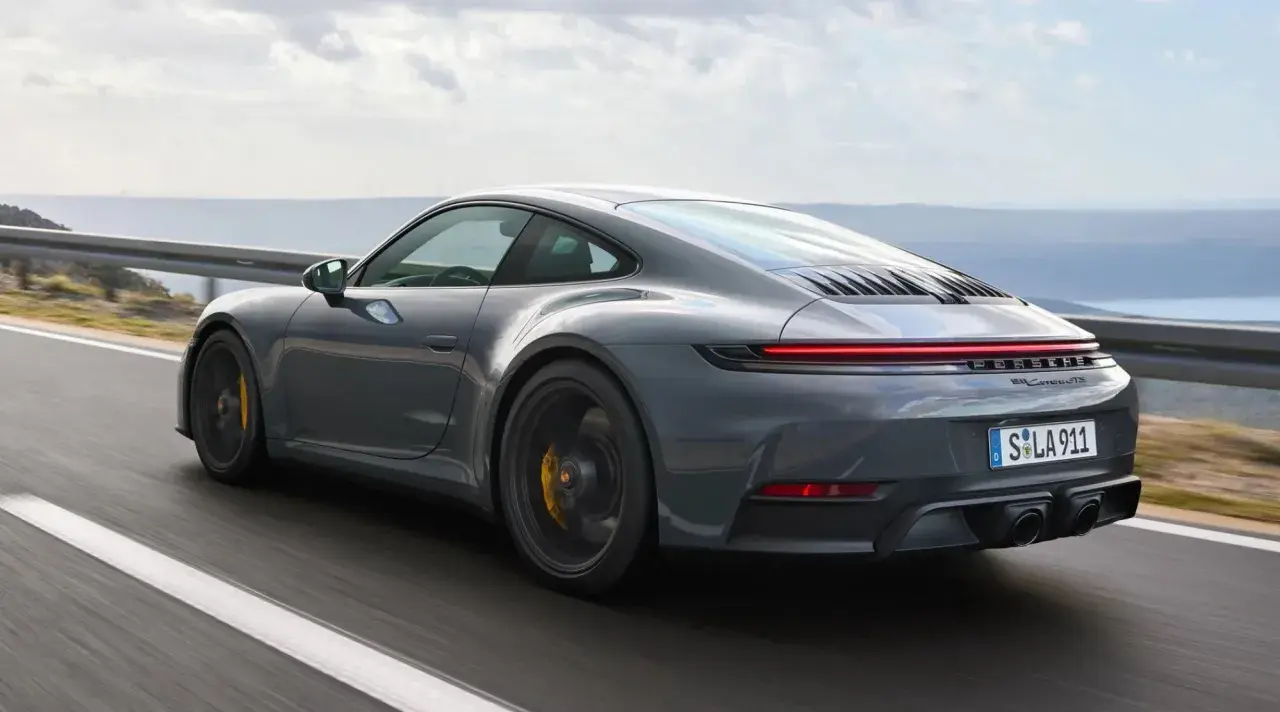 Grauer Porsche 911 Hybrid rast auf einer Küstenstraße.