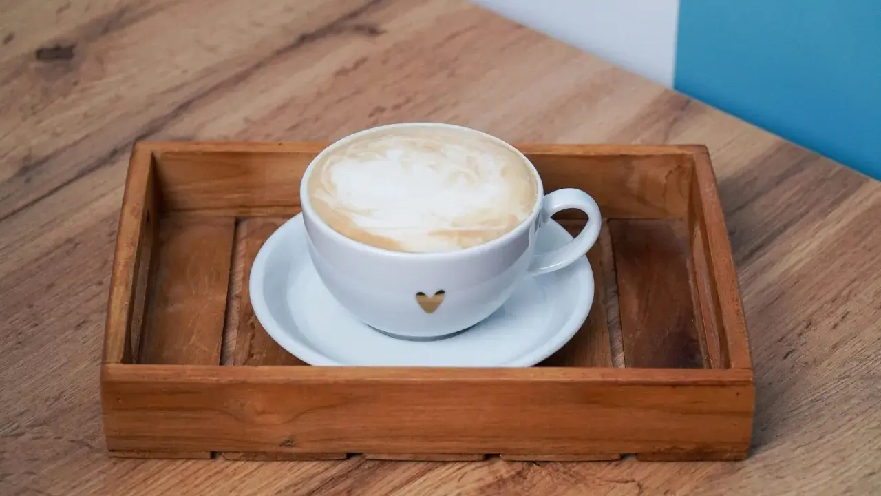 Eine Tasse Kaffee au lait mit Herz-Detail auf einem Holzteller, bereit zum Genießen.
