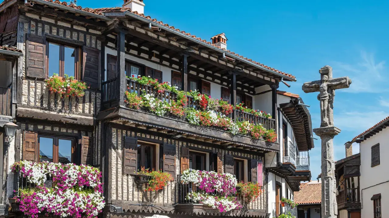 Casas de madera y piedra adornadas con flores en la Sierra de Francia. Un crucero de piedra se alza en la plaza.