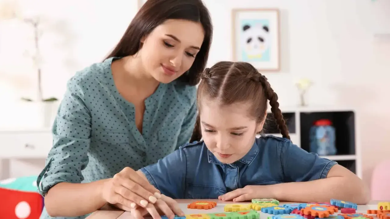 Terapeuta pomaga dziecku z niepełnosprawnością intelektualną układać kolorowe puzzle.