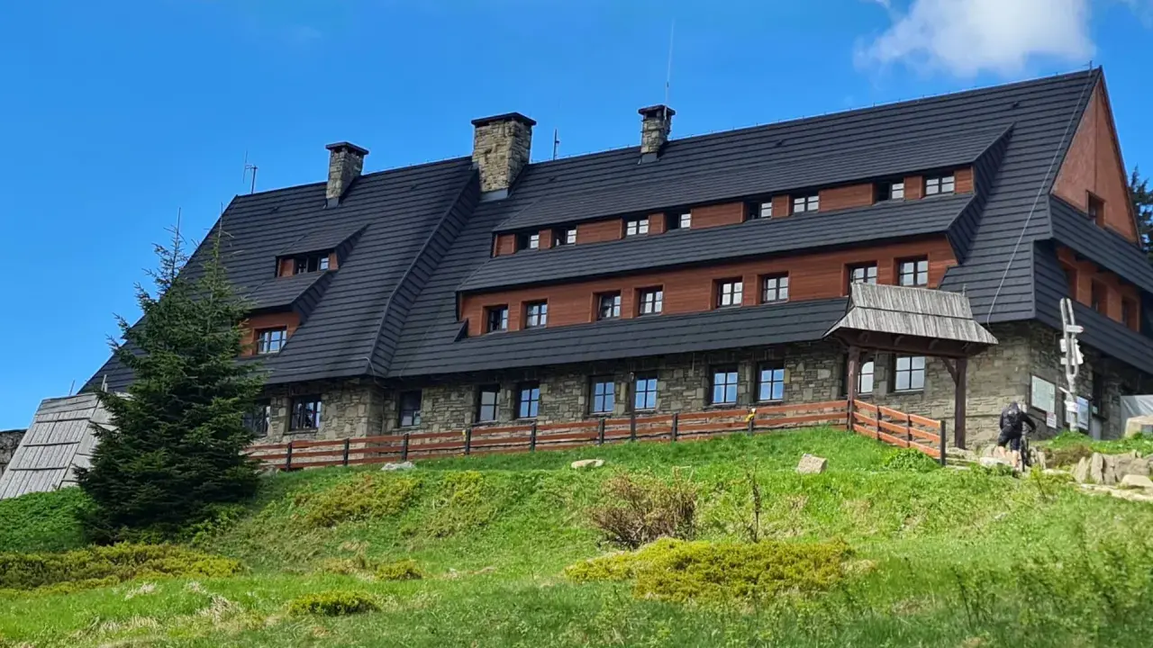 Schronisko na Turbaczu, cel wielu tras rowerowych i pieszych. Kamienno-drewniany budynek na zielonym wzgórzu.