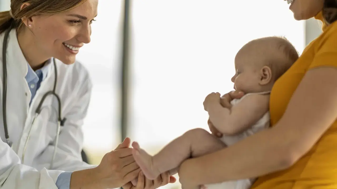 Lekarka bada niemowlę, które może mieć objawy adenowirusa. Uśmiechnięta lekarka delikatnie dotyka dłoni dziecka.