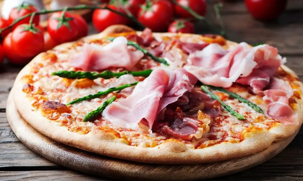 Pyszna pizza ze szparagami i szynką parmeńską, ozdobiona świeżymi pomidorkami koktajlowymi.