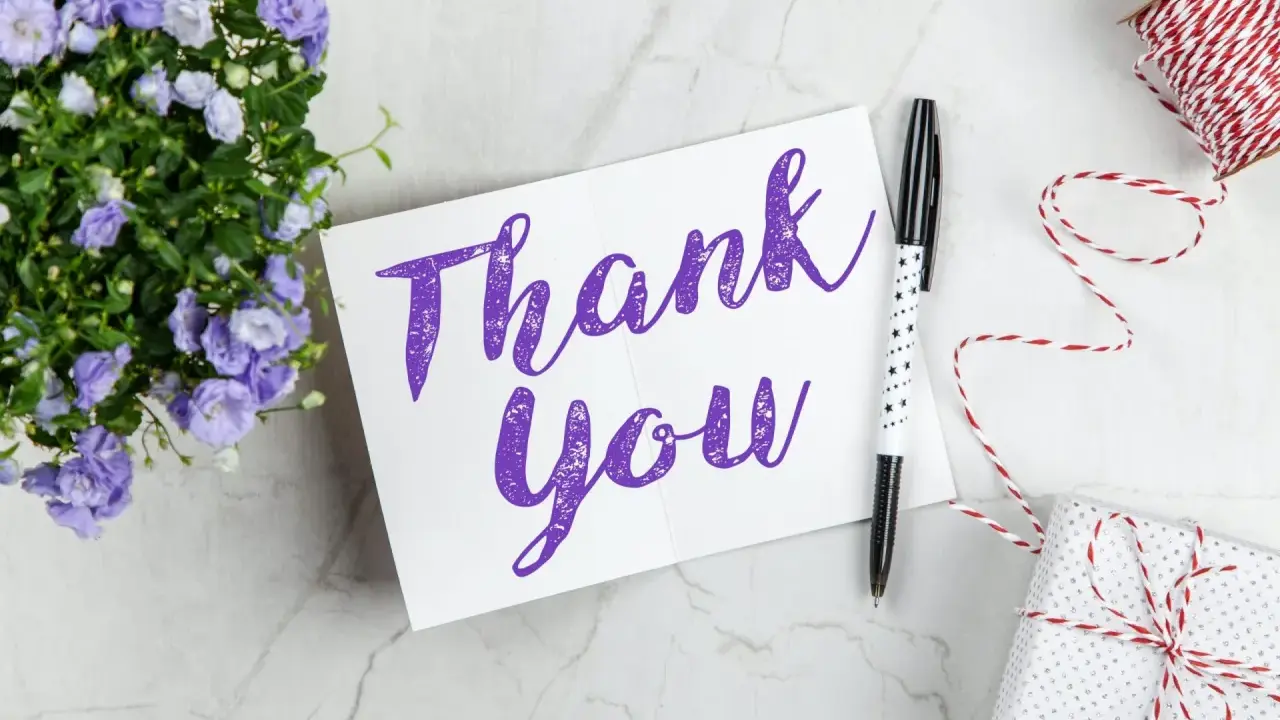 Carte "Thank You" violette, entourée de fleurs bleues, d'un stylo étoilé et d'un cadeau emballé. Une belle façon de remercier quelqu'un pour sa gentillesse.