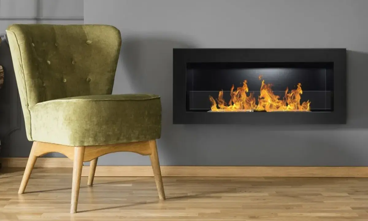 Sillón verde junto a chimenea moderna encendida. Un ejemplo de como encender la chimenea para crear un ambiente acogedor.