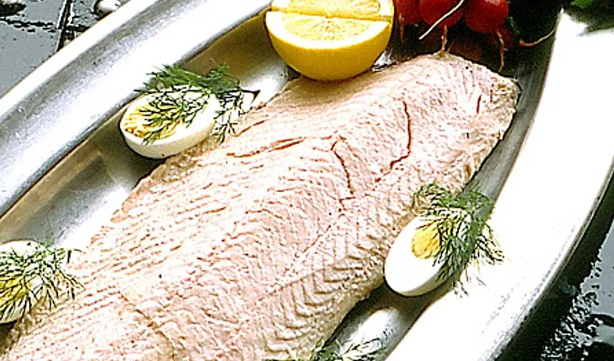 En vacker inkokt lax serveras på ett silverfat med citronklyftor, kokta ägg och dill.