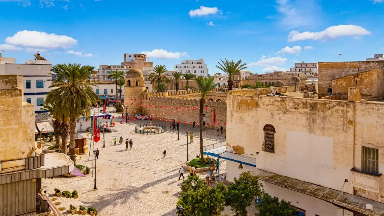 Tunezja Sousse czy warto? Rynek z palmami, zabytkową wieżą i flagami. Słoneczny dzień zachęca do zwiedzania.