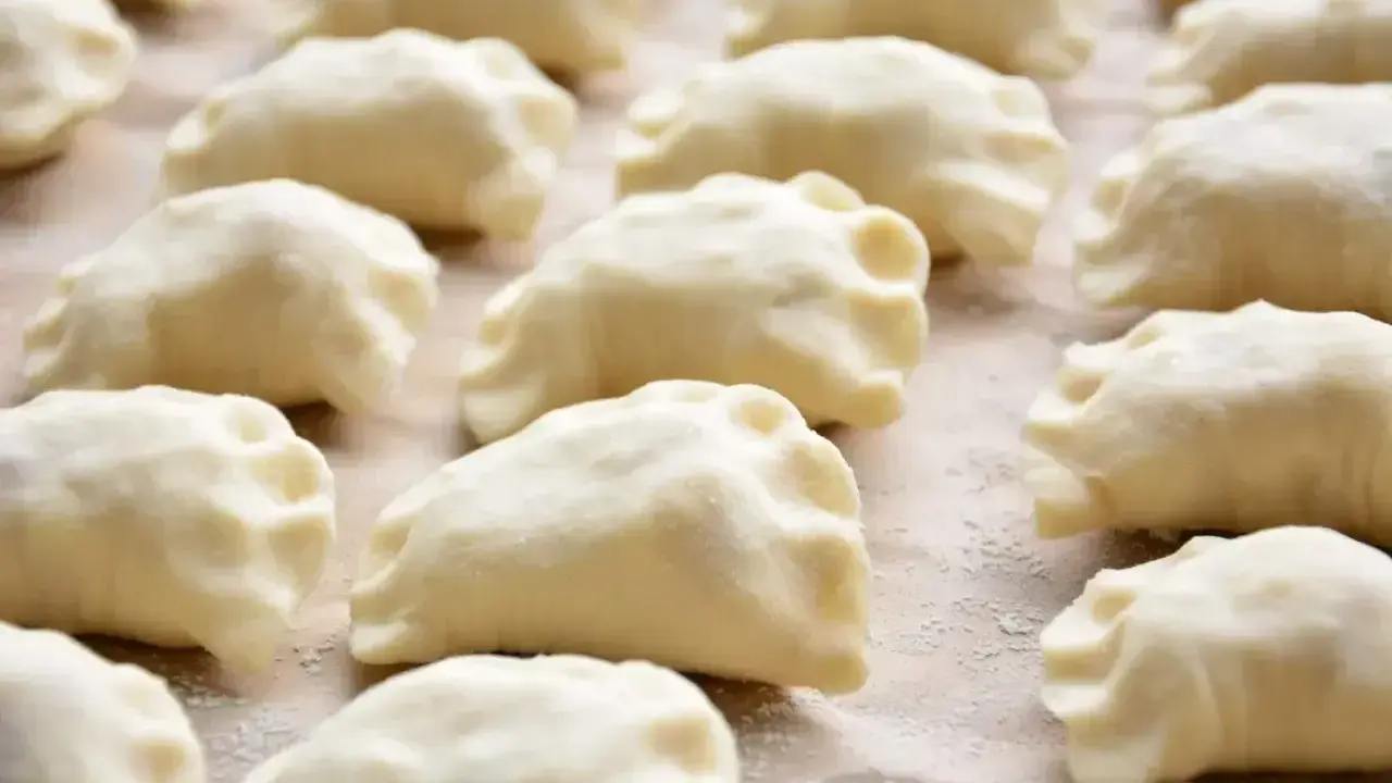 Gotowe do gotowania ciasto na pierogi, ułożone rzędami na blacie.