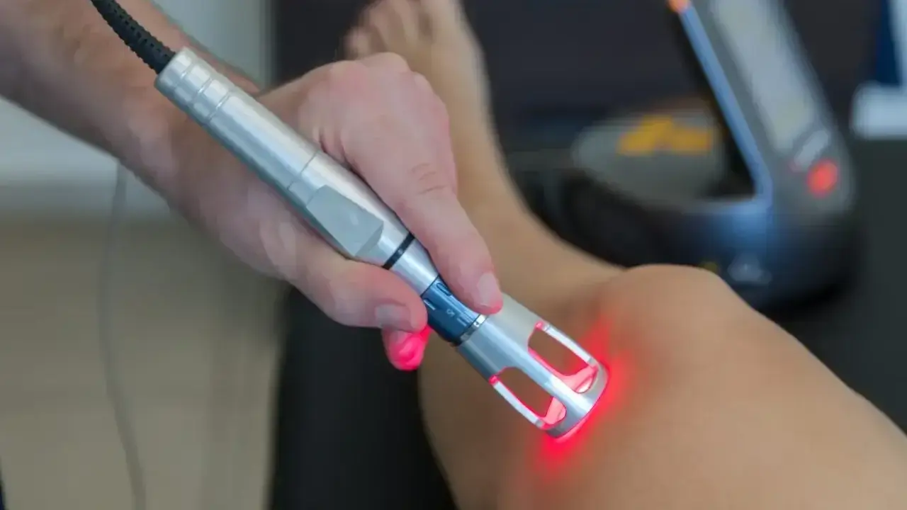 Fizjoterapeuta wykonuje laser zabieg rehabilitacyjny na kolanie pacjenta.