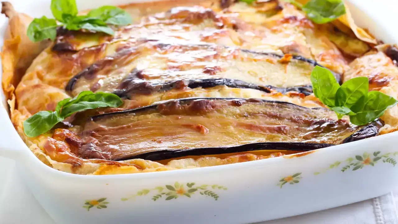 Parmigiana di melanzane napoletana recién horneada, dorada y burbujeante, decorada con hojas de albahaca fresca.