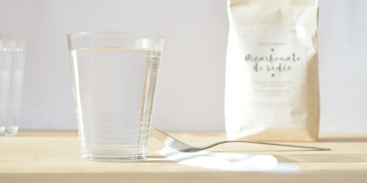 Un vaso de agua, una cuchara con bicarbonato y una bolsa de bicarbonato de sodio. ¡Listo para mezclar con vinagre!