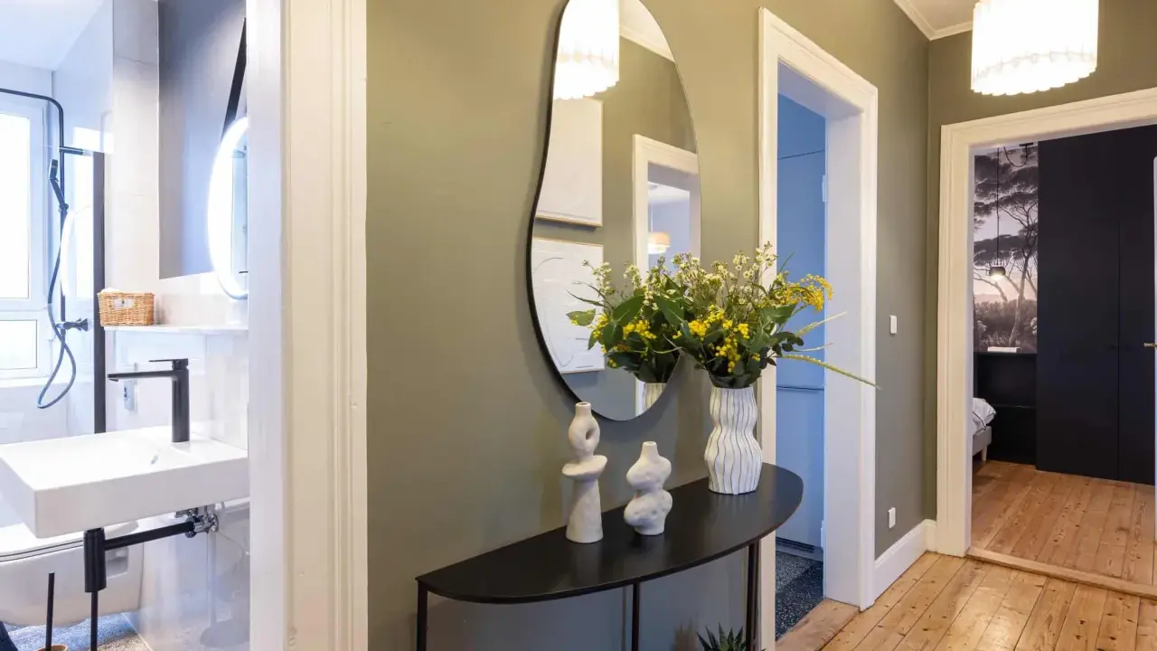 Élégant couloir maison avec miroir asymétrique, vases décoratifs, bouquet de fleurs jaunes et vue sur une salle de bain et une chambre.