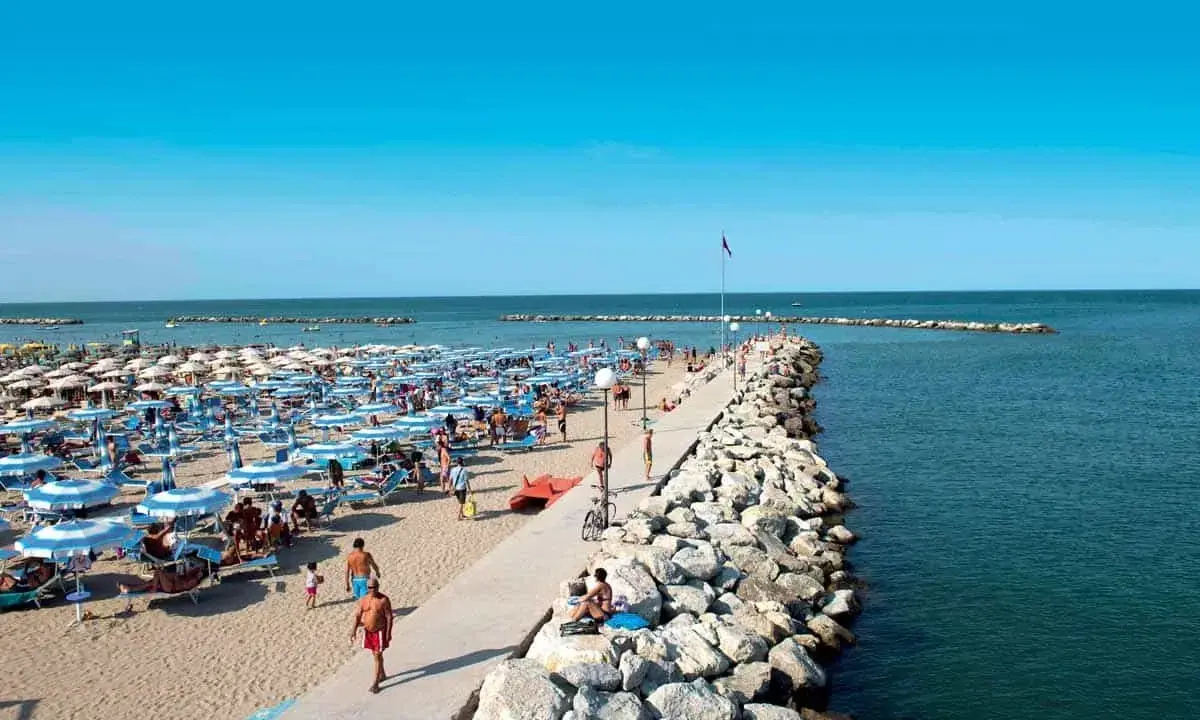 Spiaggia affollata a Gatteo Mare Cesenatico, con ombrelloni, lettini e persone che passeggiano sul molo.
