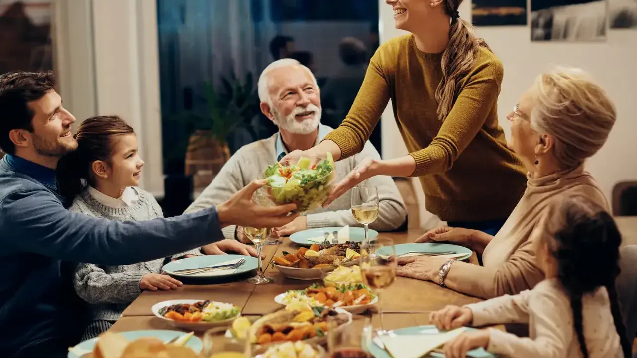 Une famille partage un repas joyeux. La mère sert la salade, et tout le monde sourit. C'est un moment de partage, alors pourquoi ne pas mettre les coudes sur la table ?