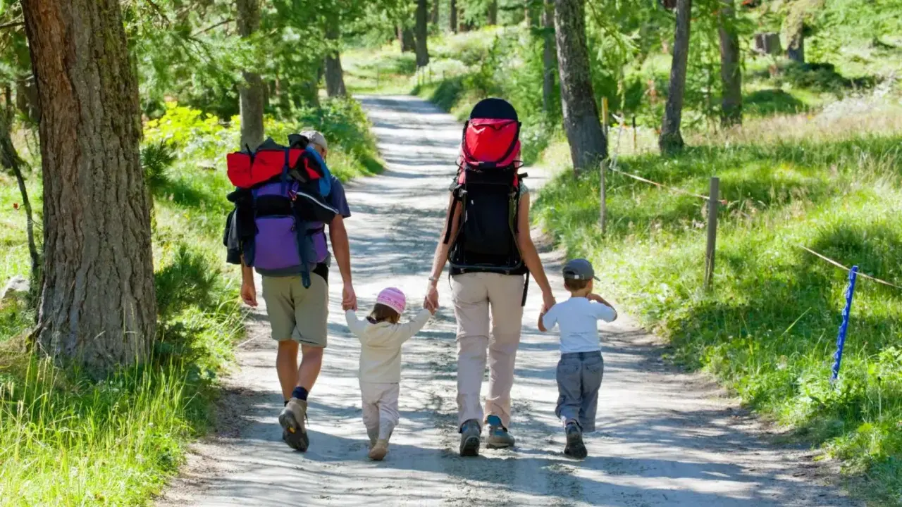 Familia con mochilas camina por un sendero boscoso, ideal para rutas para hacer con niños.