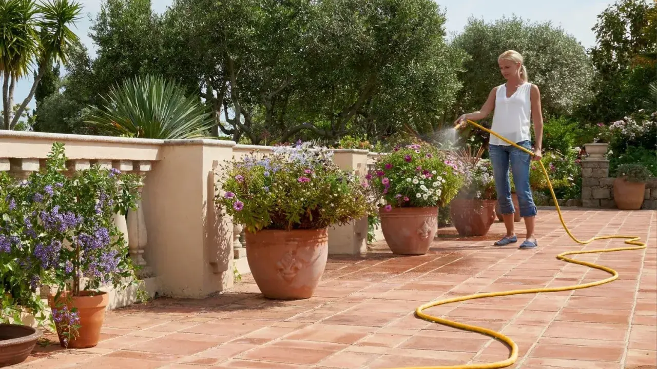 Mujer riega flores en macetas en una terraza, mostrando diferentes tipos de riego para mantenerlas sanas y vibrantes.