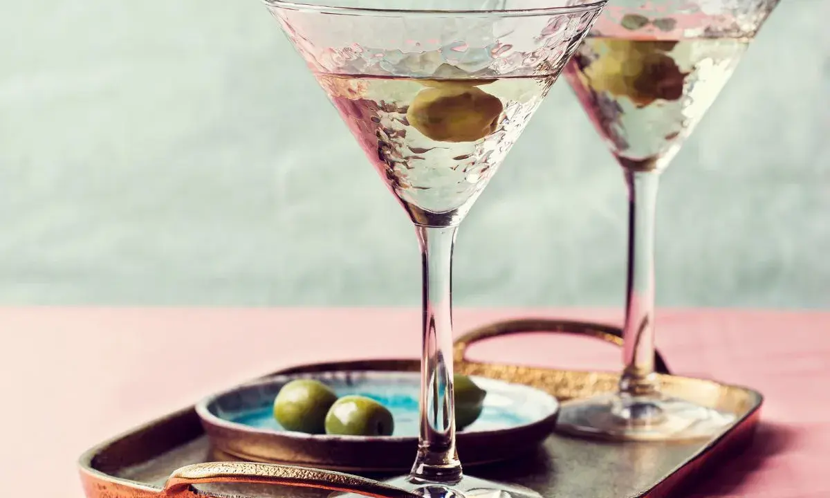 Dwa eleganckie kieliszki z domowymi drinkami z martini, ozdobione oliwkami, na tacy z przekąskami.