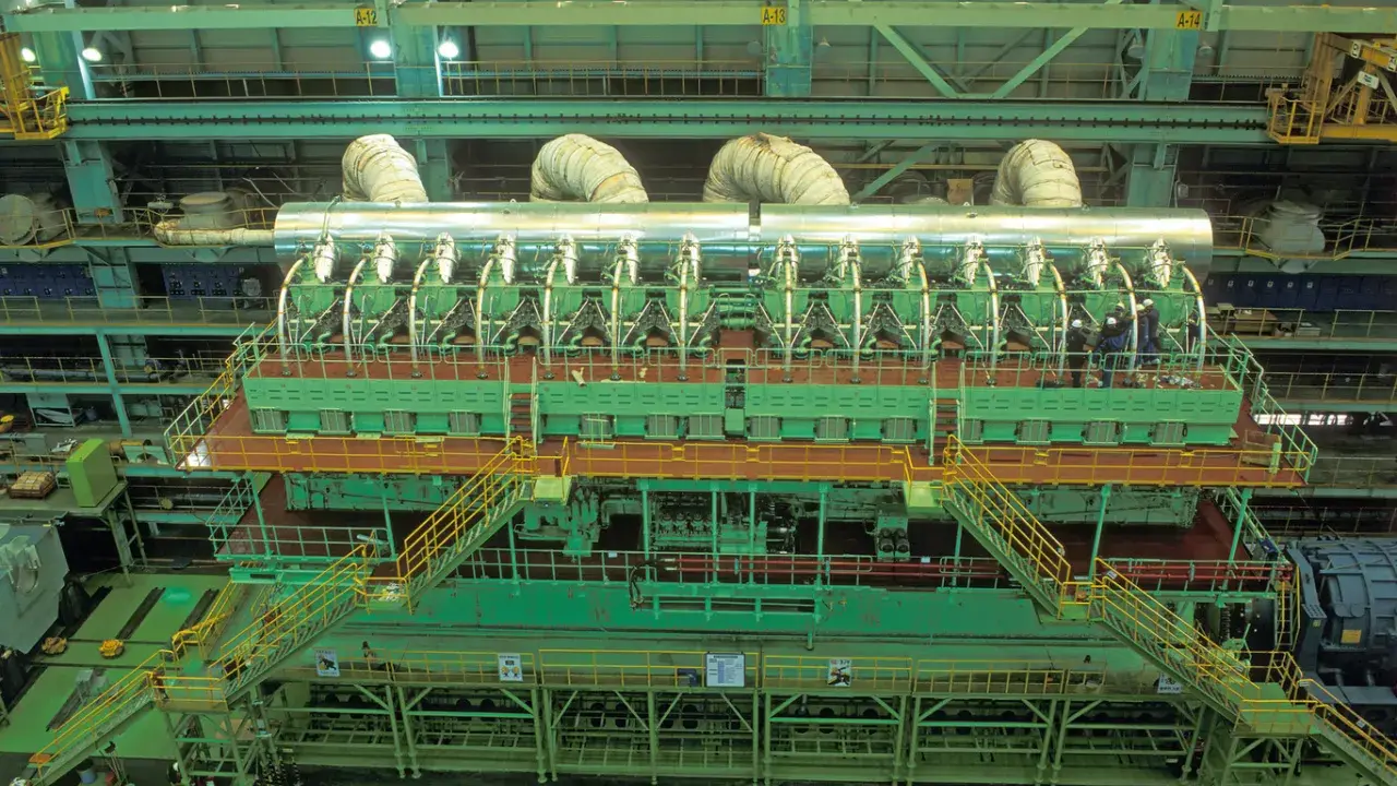 Vue aérienne d'un moteur de bateau massif, le plus gros moteur de bateau jamais construit, avec des ouvriers inspectant son imposante structure verte et argentée.