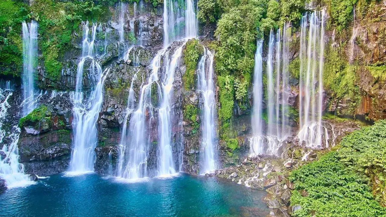 Vackra vattenfall kaskaderar nerför klippor täckta av frodig grönska, ner i en turkos lagun. En idyllisk plats nära Saint-Denis.