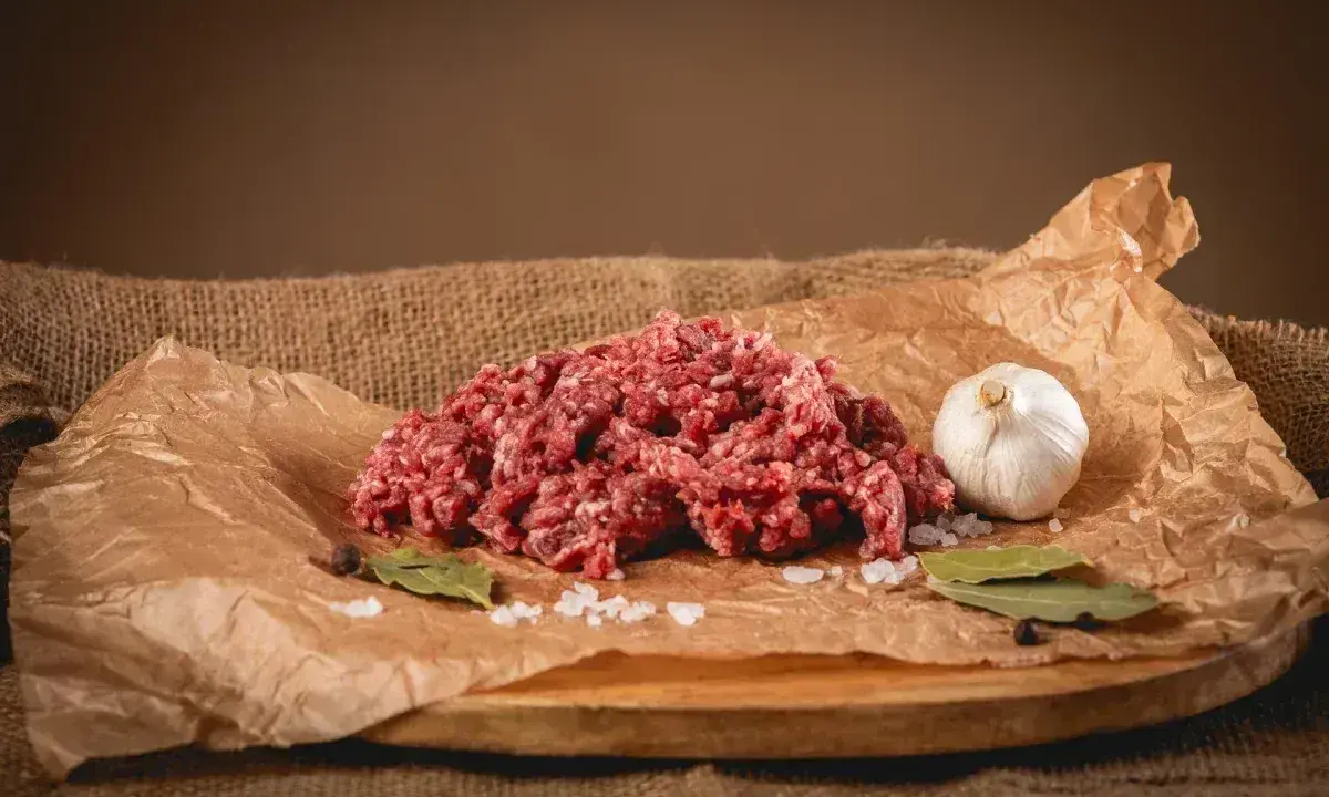 Surowe mielone mięso, idealne na soczyste burgery. Obok czosnek, liście laurowe i sól.