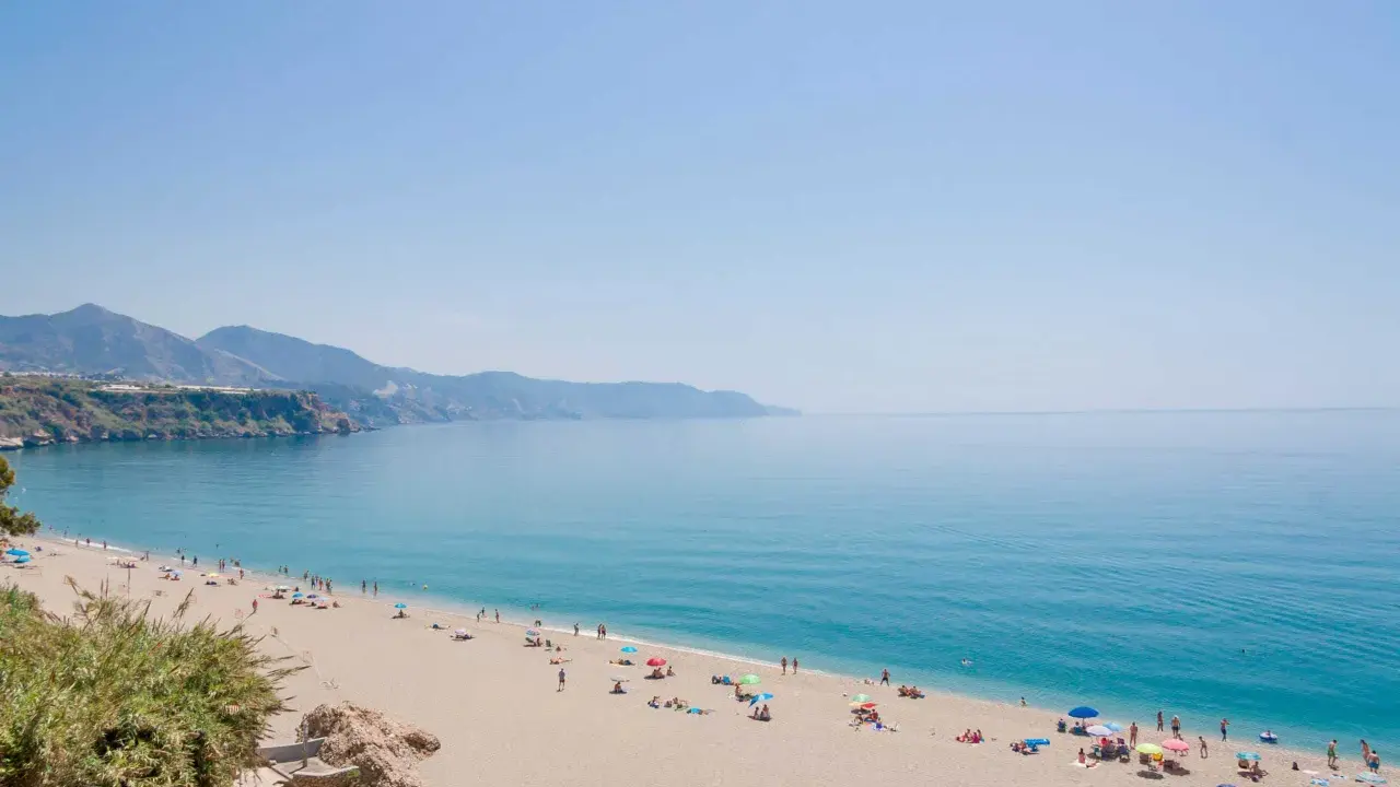 Sonniger malaga strand mit vielen Menschen, die sich unter bunten Sonnenschirmen entspannen. Das türkisfarbene Meer lädt zum Baden ein.