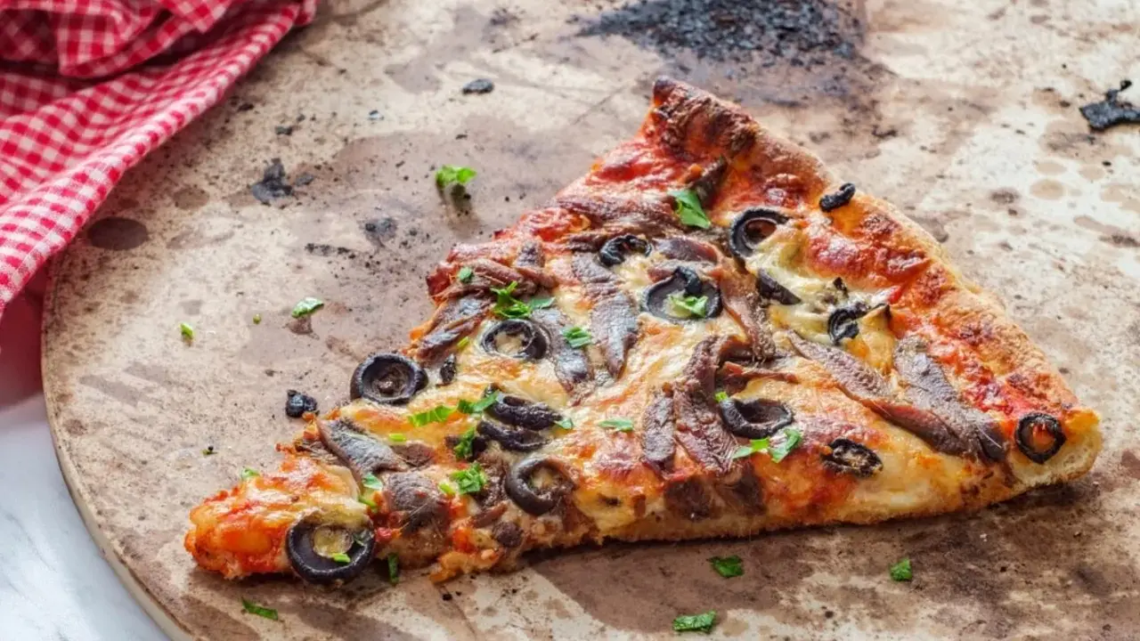 Une part de pizza aux anchois et olives sur une pierre réfractaire, prête pour un nettoyage.