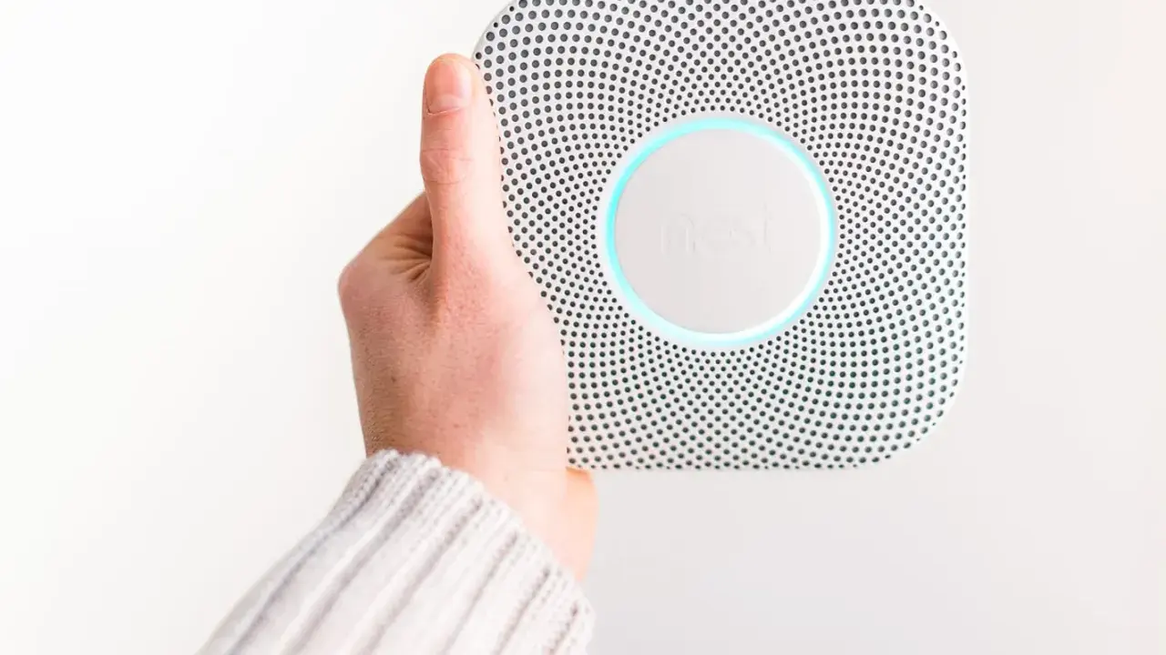 En hand håller upp en vit Google Nest Protect-rökdetektor med blåaktig glöd.