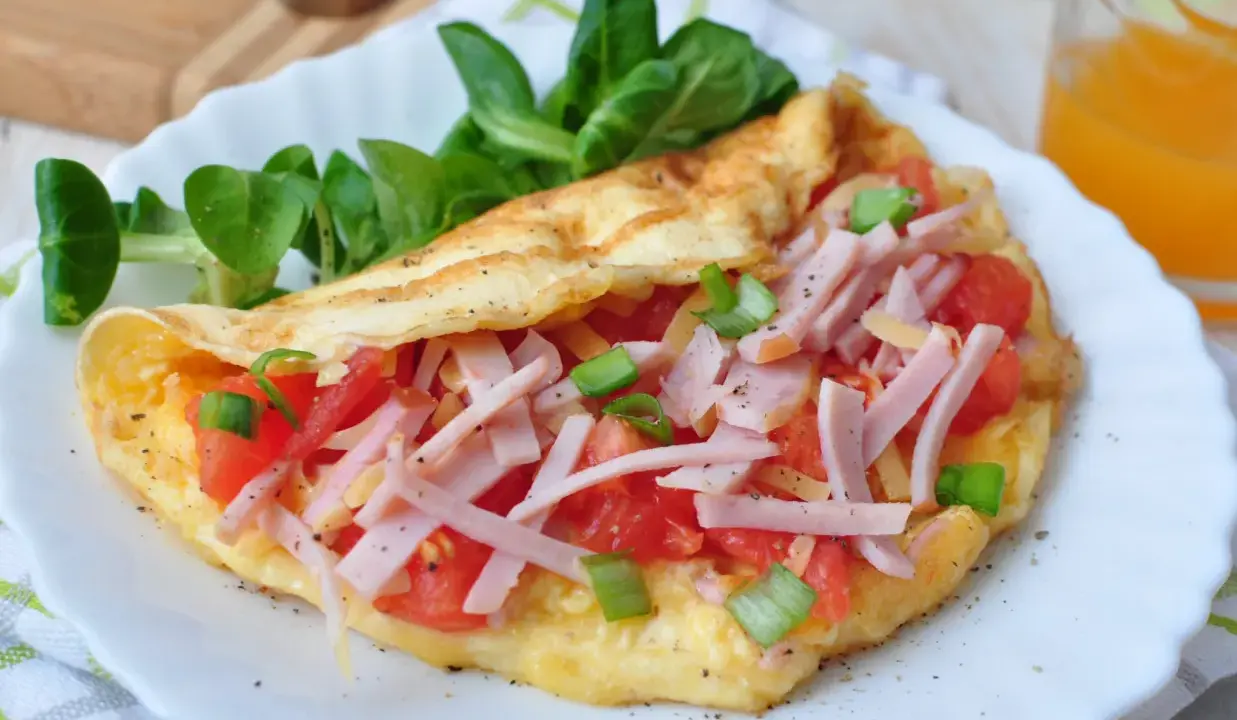 Pyszny omlet bez mąki z szynką, pomidorami i szczypiorkiem, podany z sałatką. Idealny na szybkie śniadanie.