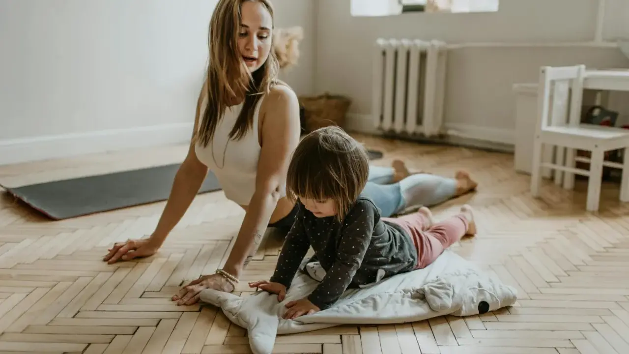 Mama uczy dziecko nauki oddychania podczas ćwiczeń jogi. Dziecko leży na poduszce w kształcie rekina, a mama w pozycji kobry.