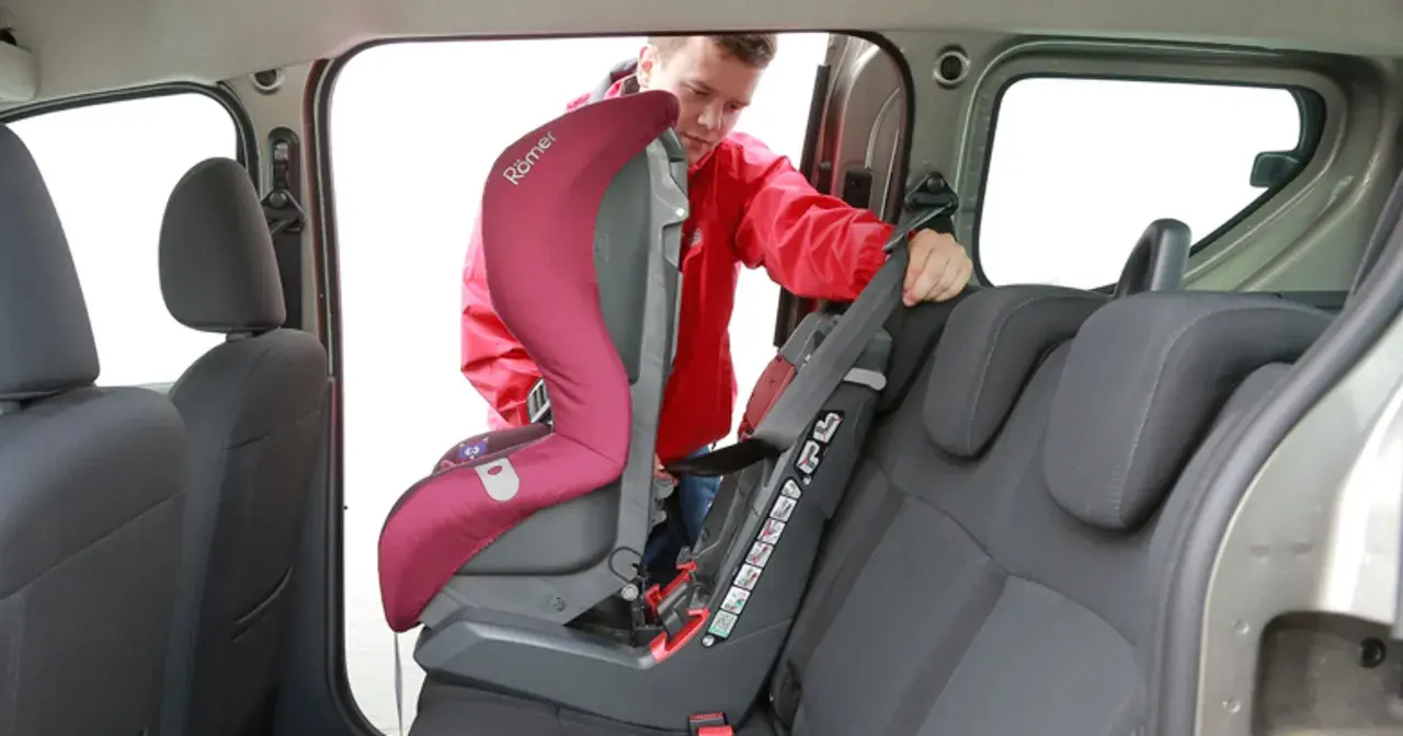 Mężczyzna montuje fotelik samochodowy. Sprawdź, jak sprawdzić, czy samochód ma isofix, patrząc na zaczepy fotelika.