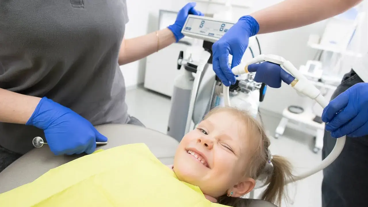 Uśmiechnięta dziewczynka na fotelu dentystycznym, przygotowywana do zabiegu z użyciem sedacji wziewnej.