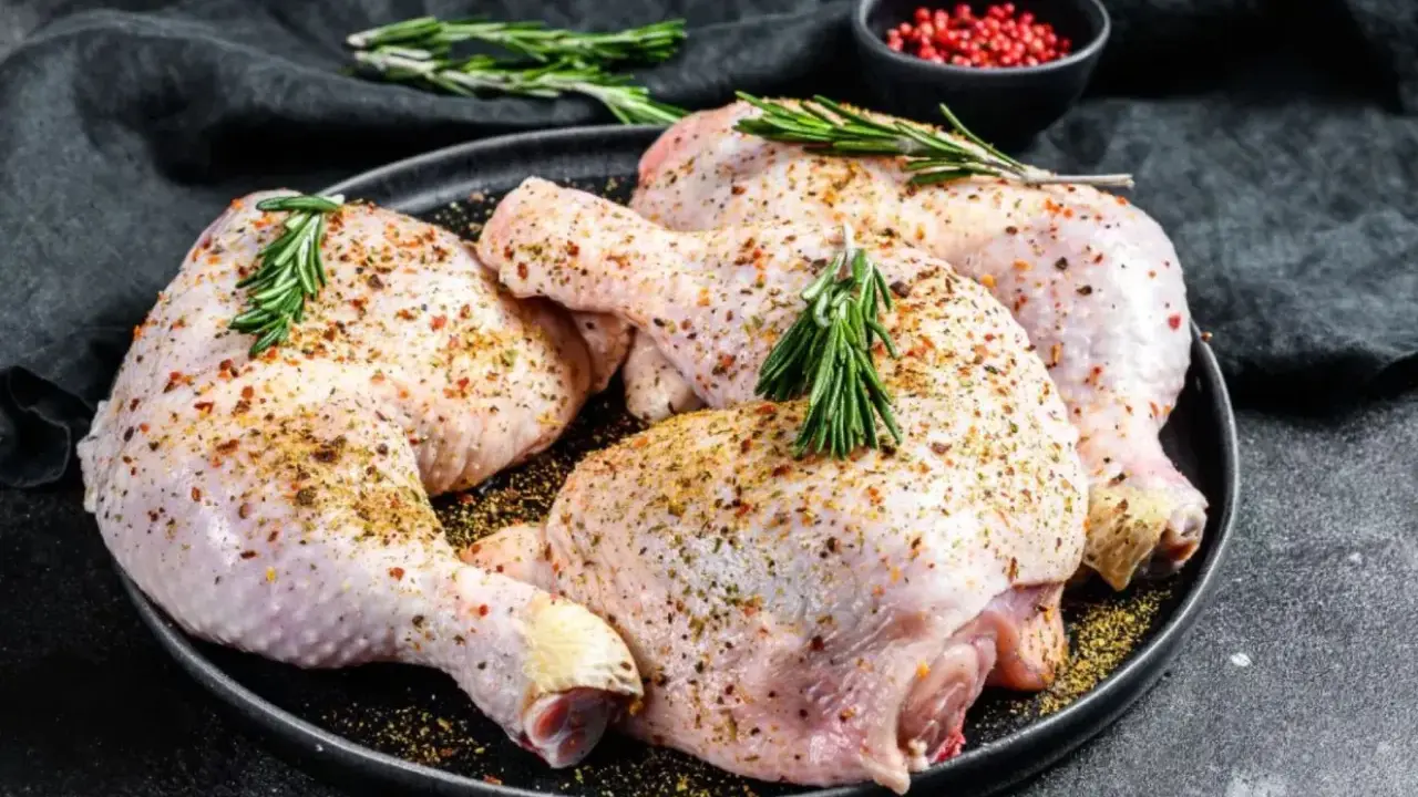 Quatre cuisses de poulet crues, assaisonnées et garnies de romarin, prêtes pour une marinade poulet savoureuse.