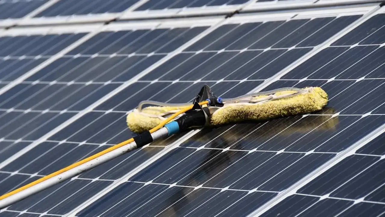 Reinigung von Solaranlagen mit einem Teleskopwischer. Gelber Wischerkopf auf dunklen Solarzellen.