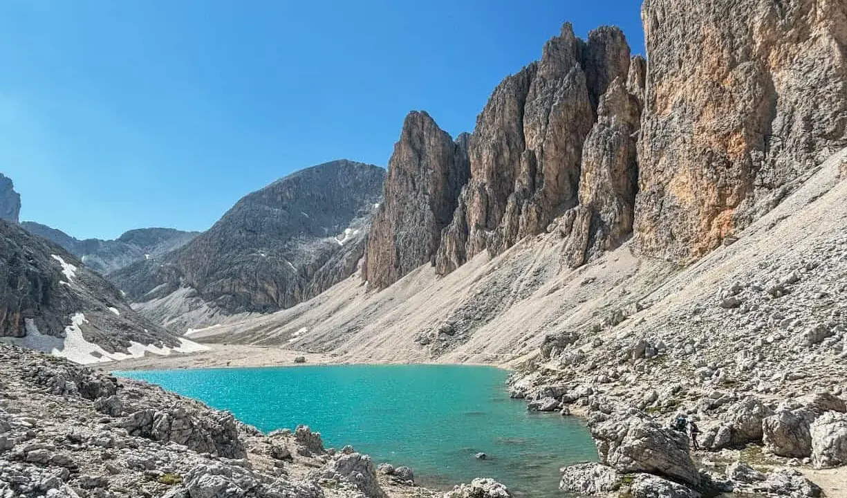 Il **lago di Antermoia**, incastonato tra imponenti pareti rocciose, brilla di un turchese intenso sotto un cielo azzurro.