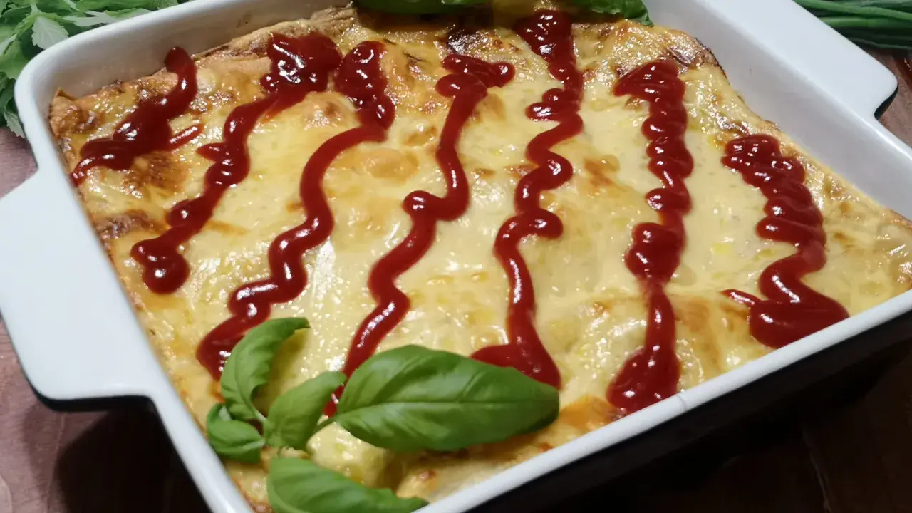 Pyszne, zapieczone fit lasagne w białym naczyniu, polane ketchupem i ozdobione listkami bazylii.
