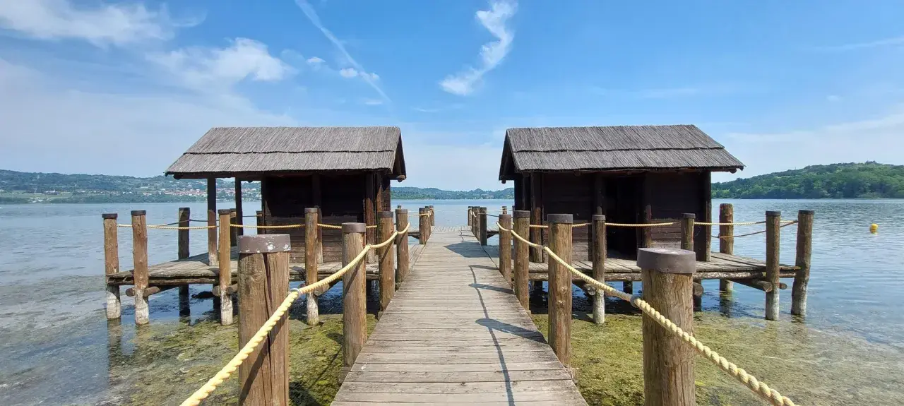 Pontile in legno con due capanne sul lago di Viverone, sotto un cielo azzurro con nuvole bianche.