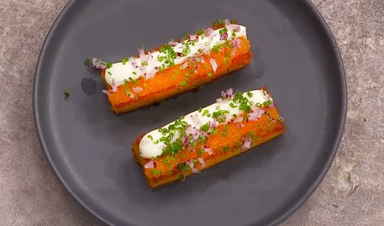 Två gyllene, rektangulära tater tots toppas med gräddfil, finhackad rödlök och gräslök.